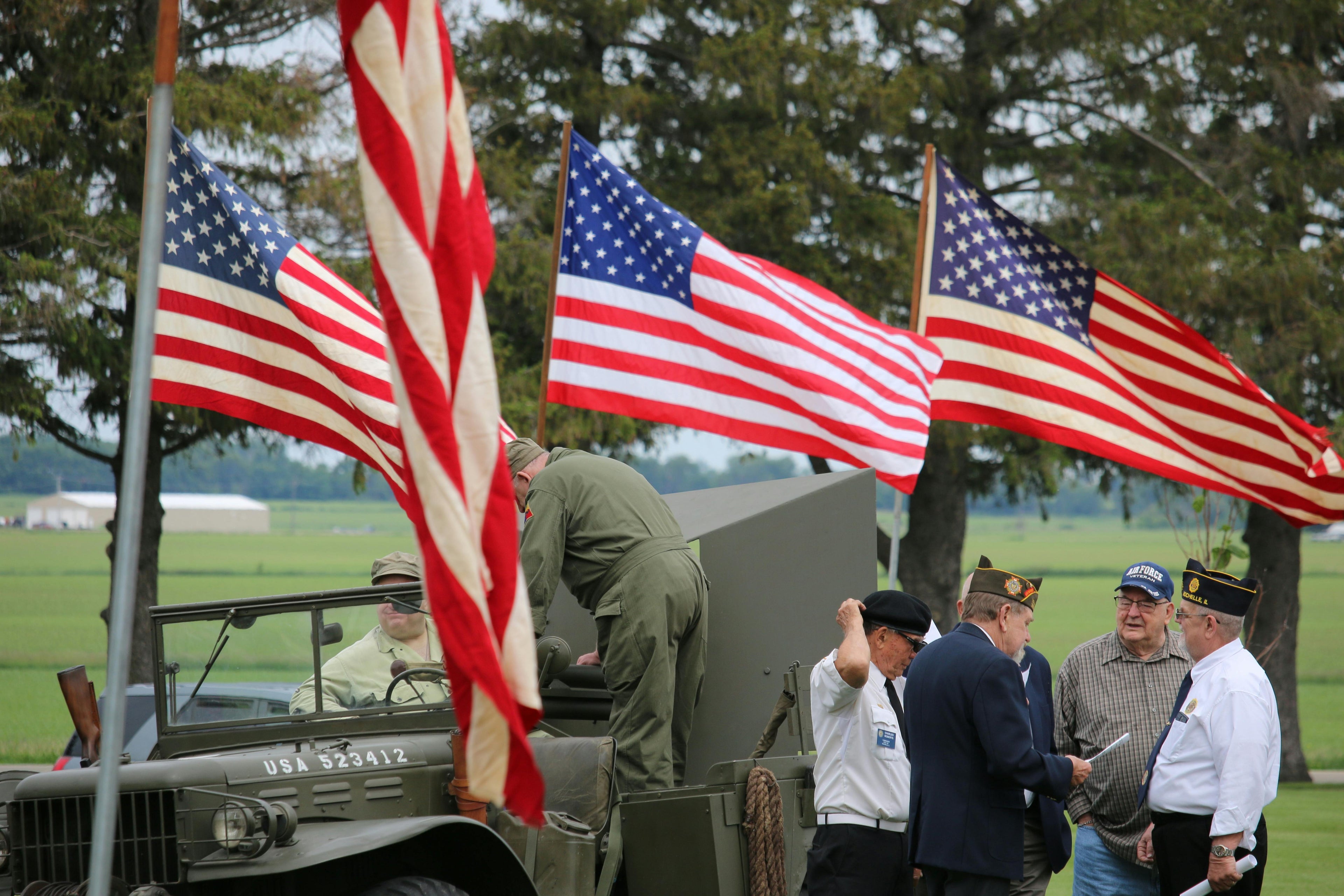 Group of people with American flags in a field with a military vehicle.