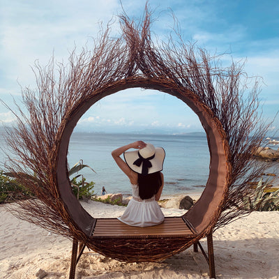 Person sitting on a circular wicker chair with a beach view